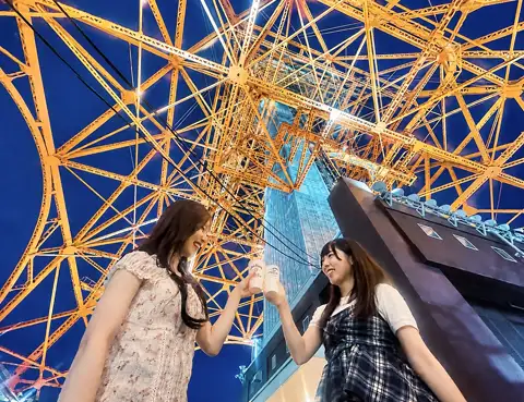 オレンジ色にライトアップされた東京タワーの鉄骨を見上げながら、飲み物を口にする2人の女性