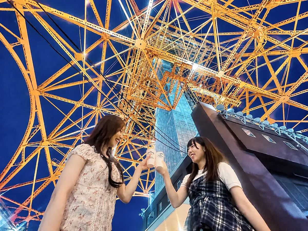 オレンジ色にライトアップされた東京タワーの鉄骨を見上げながら、飲み物を口にする2人の女性