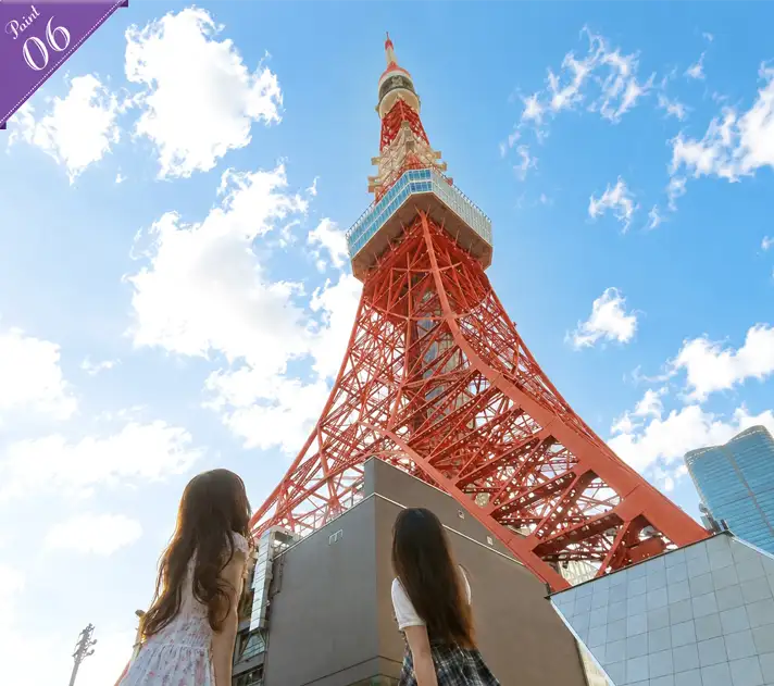青空に向かって高くそびえ立つ東京タワーの足元を見上げる2人の女性の後ろ姿