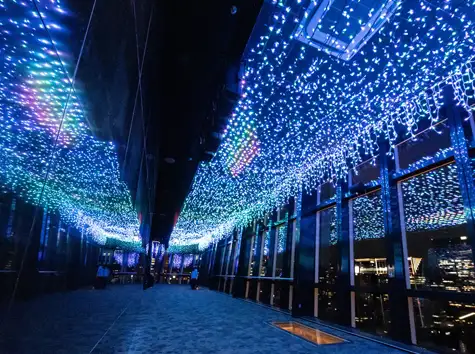 青い光のイルミネーションが天井一面に広がる、東京の夜景を望むメインデッキの通路