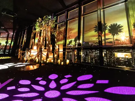 紫や黄色の花柄プロジェクションマッピングが床や窓に映し出された、夕暮れ時のメインデッキ