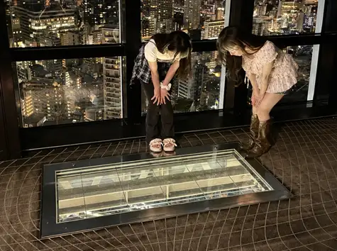 ガラス張りのスカイウォークウィンドウ越しに、夜景を見下ろしながら覗き込む2人の女性