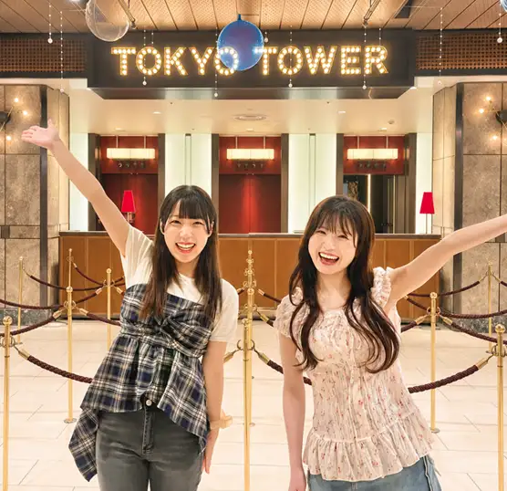 輝く「TOKYO TOWER」のサインの前でガッツポーズをして喜ぶ2人の女性