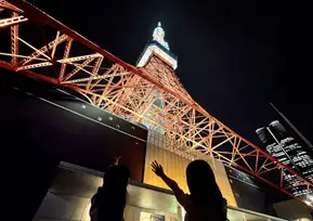 オレンジ色にライトアップされた東京タワーを見上げ、手を振る2人の女性のシルエット